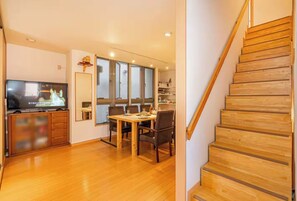 A modern living room with a wooden staircase, a dining area with a table and chairs, and a TV on a wooden cabinet. - Asakusa hanabi (Tokyo)