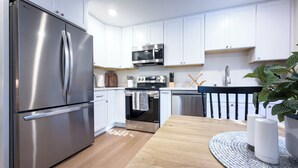 Eine moderne Küche mit weißen Schränken, Edelstahlgeräten, einem Holztisch und einem Blumentopf.