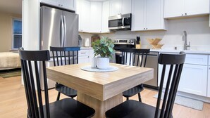 Eine moderne Küche mit weißen Schränken, Edelstahlgeräten und einem Essbereich mit einem Holztisch und schwarzen Stühlen.
