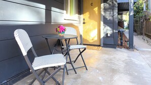 Eine Terrasse mit zwei Stühlen und einem Tisch, eine Tür mit dem Buchstaben 'C' und ein kleiner Gartenbereich.