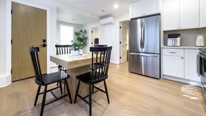 Eine moderne Küche mit einem Edelstahl-Kühlschrank, weißen Schränken und einem Holzespeisetisch mit schwarzen Stühlen.