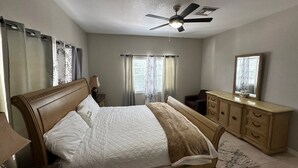 Ein Schlafzimmer mit einem Bett, einem Schminktisch, einem Spiegel, einem Deckenventilator und Vorhängen.