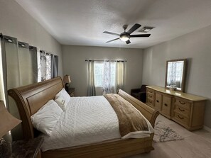 Un dormitorio con cama, cómoda, espejo, ventilador de techo y cortinas.
