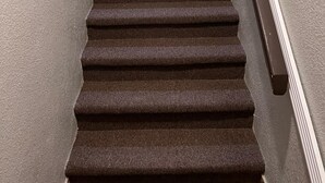 Ein Teppich mit einer Treppe, rechts eine Handläufe.