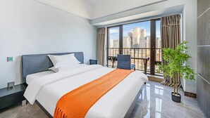 A modern hotel room with a large bed, a balcony with a city view, and a potted plant. - Shengmei Ya International Apartment  (Guangzhou)