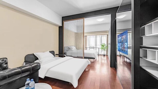 A modern hotel room with a bed, a seating area with a table, and a TV. - Shengmei Ya International Apartment  (Guangzhou)