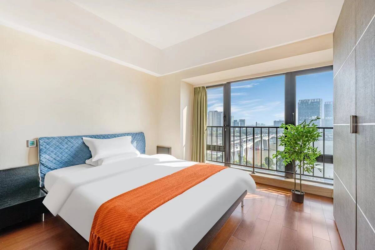 Ein Hotelzimmer mit einem großen Bett, Blick auf die Stadt durch einen Balkon und einer Zimmerpflanze.