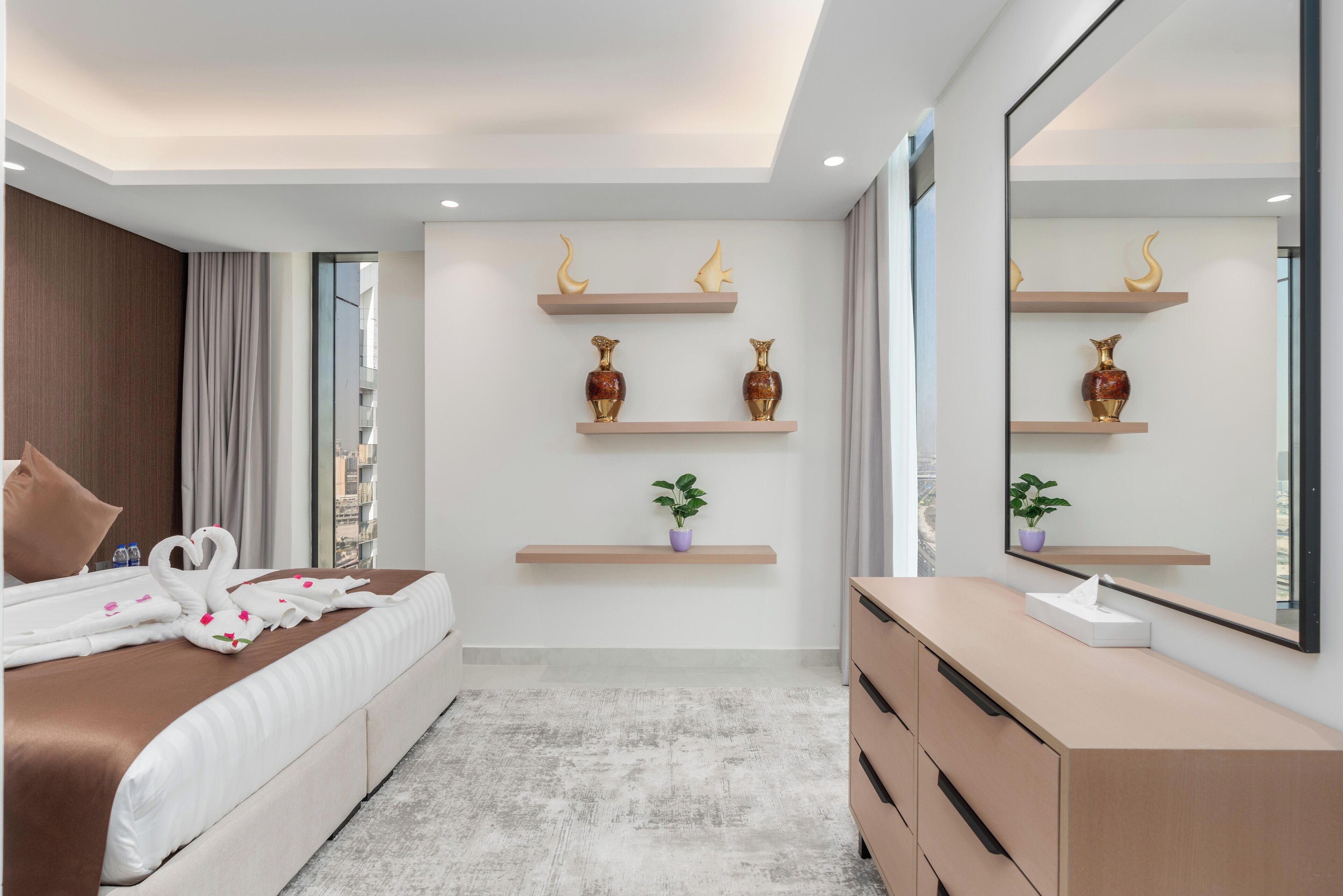 A modern hotel room with a large bed, a vanity with a mirror, and decorative wall shelves.