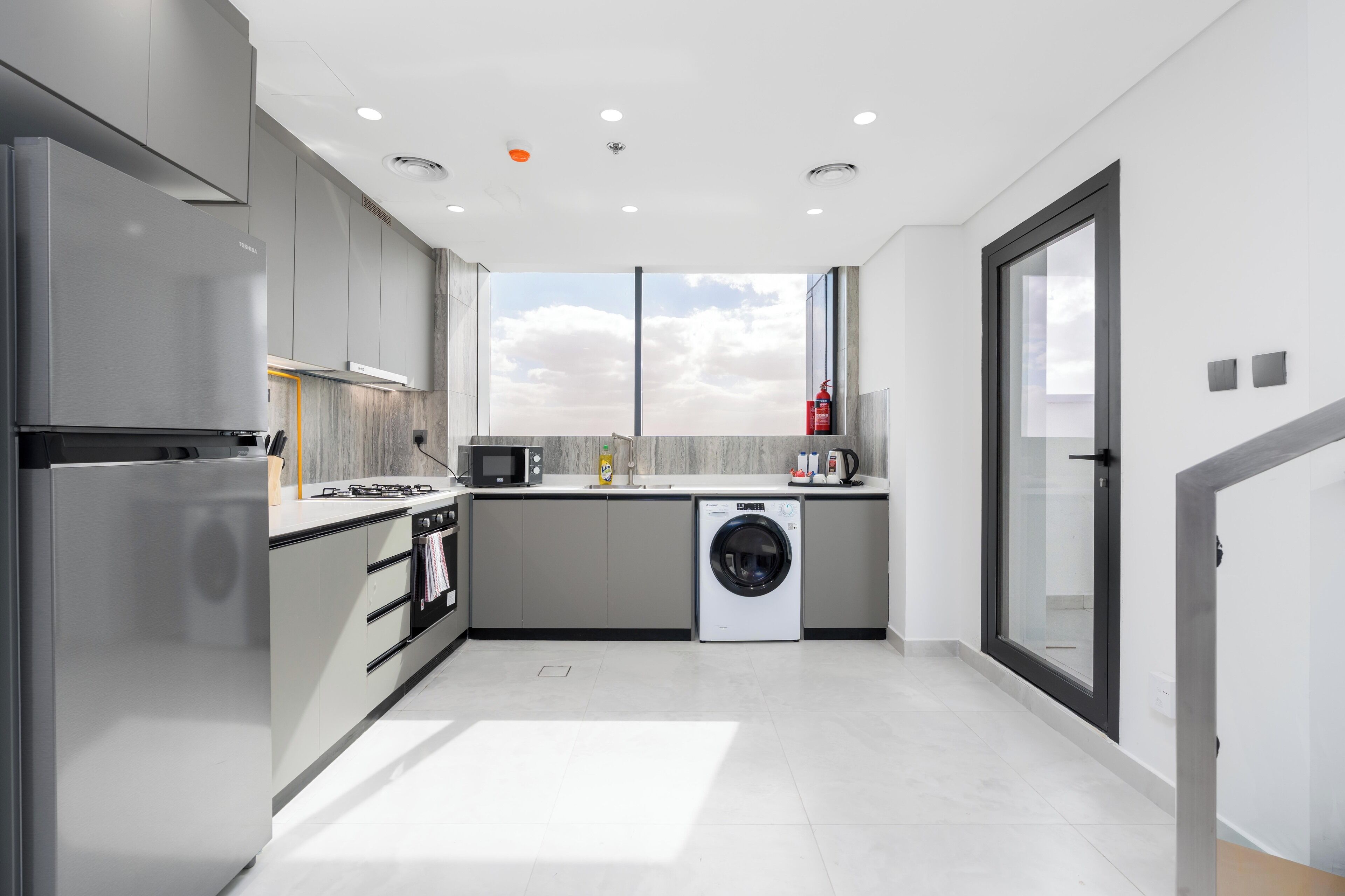Una cucina moderna con elettrodomestici in acciaio inossidabile, una lavatrice integrata e un'ampia finestra che offre vista sul cielo.