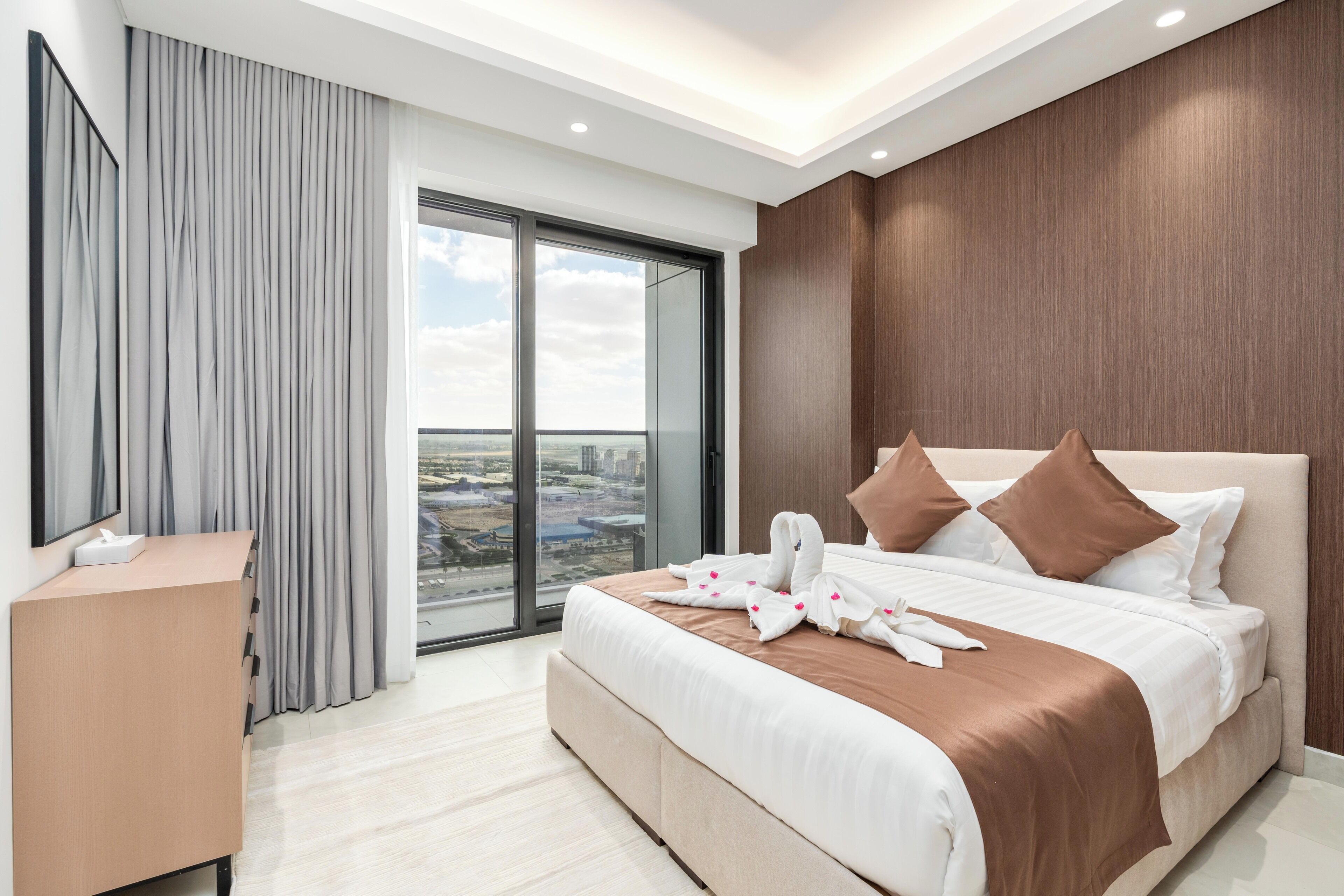 Ein modernes Hotelzimmer mit einem großen Bett, einem Schreibtisch und Blick auf die Stadt durch raumhohe Fenster.