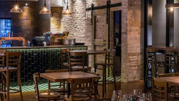 Interior de restaurante con paredes de ladrillo, lámparas colgantes y mesas y sillas de madera.