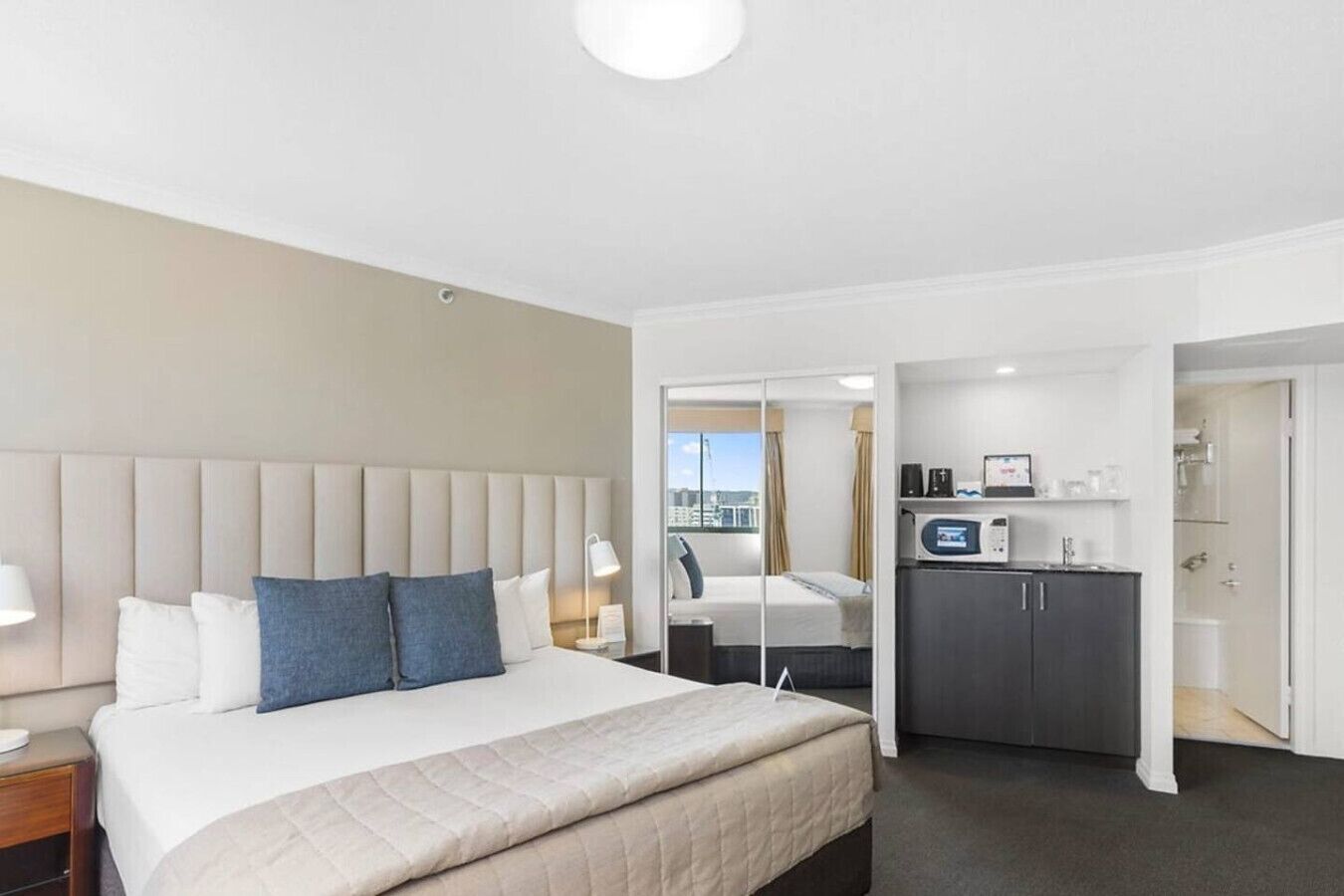 A hotel room with a large bed, a desk, a kitchenette, and a bathroom.
