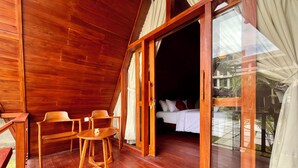 A wooden cabin with a balcony, a bed with white bedding, and a small wooden table and chairs. - Dalung Tropical (Dalung)