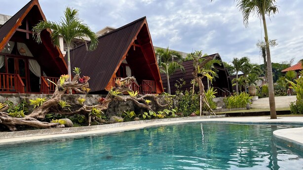 A pool area with clear water, surrounded by tropical plants and wooden structures. - Dalung Tropical (Dalung)