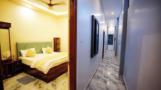 A hotel room with a bed, bedside table, and a mirror. A hallway with a marble floor leads to another room. - BKV Rooms (Varanasi)
