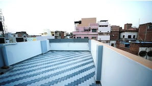 Eine Dachterrasse mit gemusterten Fliesen, einer weißen Wand und umgebenden Gebäuden.