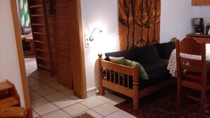 Een gezellige woonkamer met een houten bank, een vloerkleed met dessin en een groot wandtapijt.