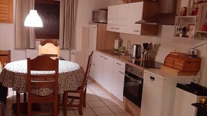 Een kleine keuken met een ronde eettafel, houten stoelen, een magnetron, een fornuis en een vaatwasser.