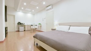 Une chambre d’hôtel moderne dotée d’un grand lit, d’un bureau avec une chaise, d’une kitchenette et d’un climatiseur fixé au plafond.