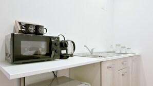 Une petite cuisine équipée d’un four à micro-ondes, d’une bouilloire et d’une machine à café, le tout posé sur un plan de travail blanc.