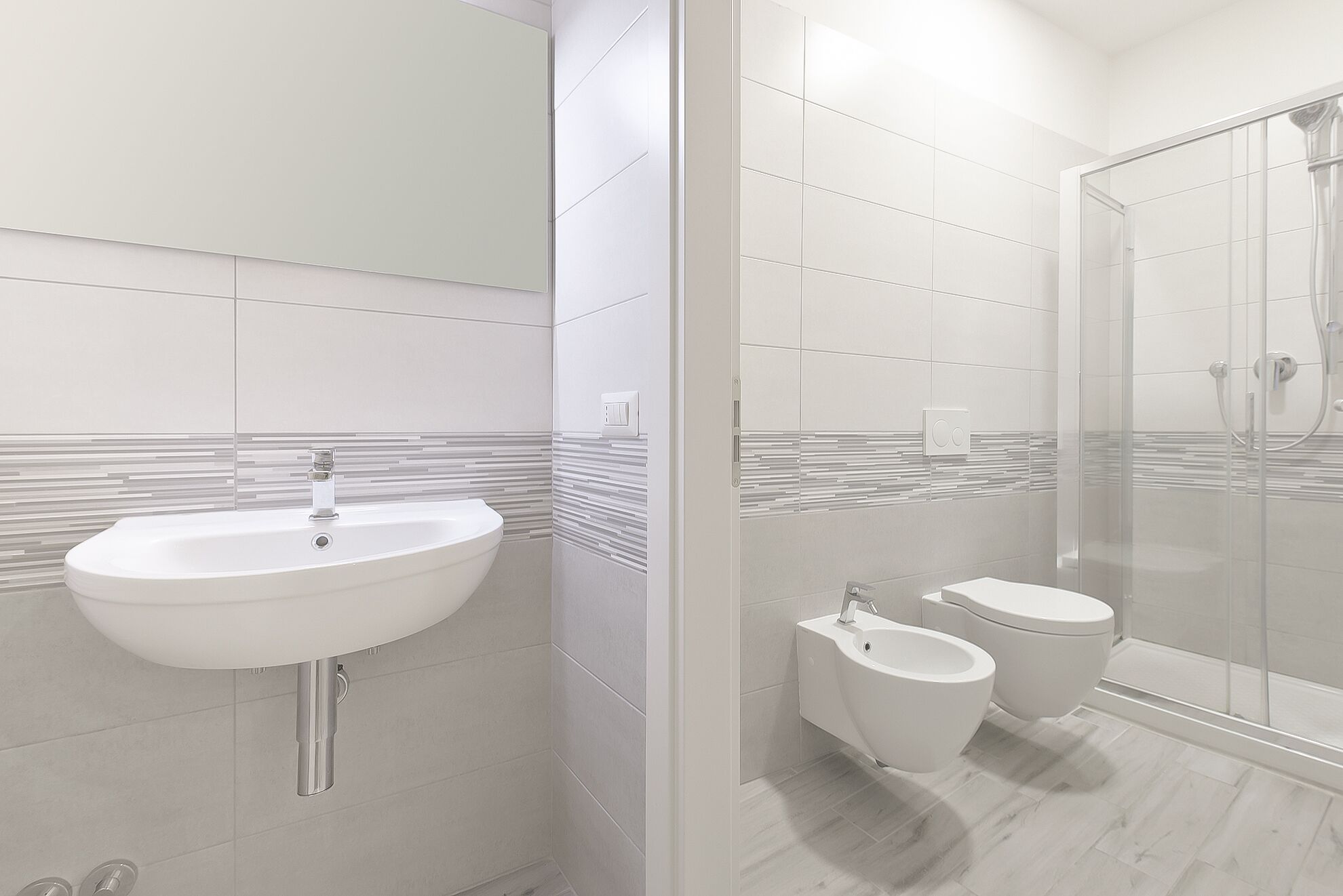 A modern bathroom with a white sink, toilet, and bidet, a glass shower enclosure, and a mirror above the sink.