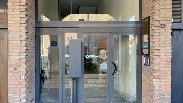Une entrée moderne avec des portes en verre, une poignée en métal et une façade en briques.