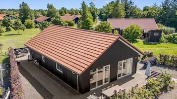 A single-story building with a sloped roof, large windows, and a patio area with outdoor furniture.