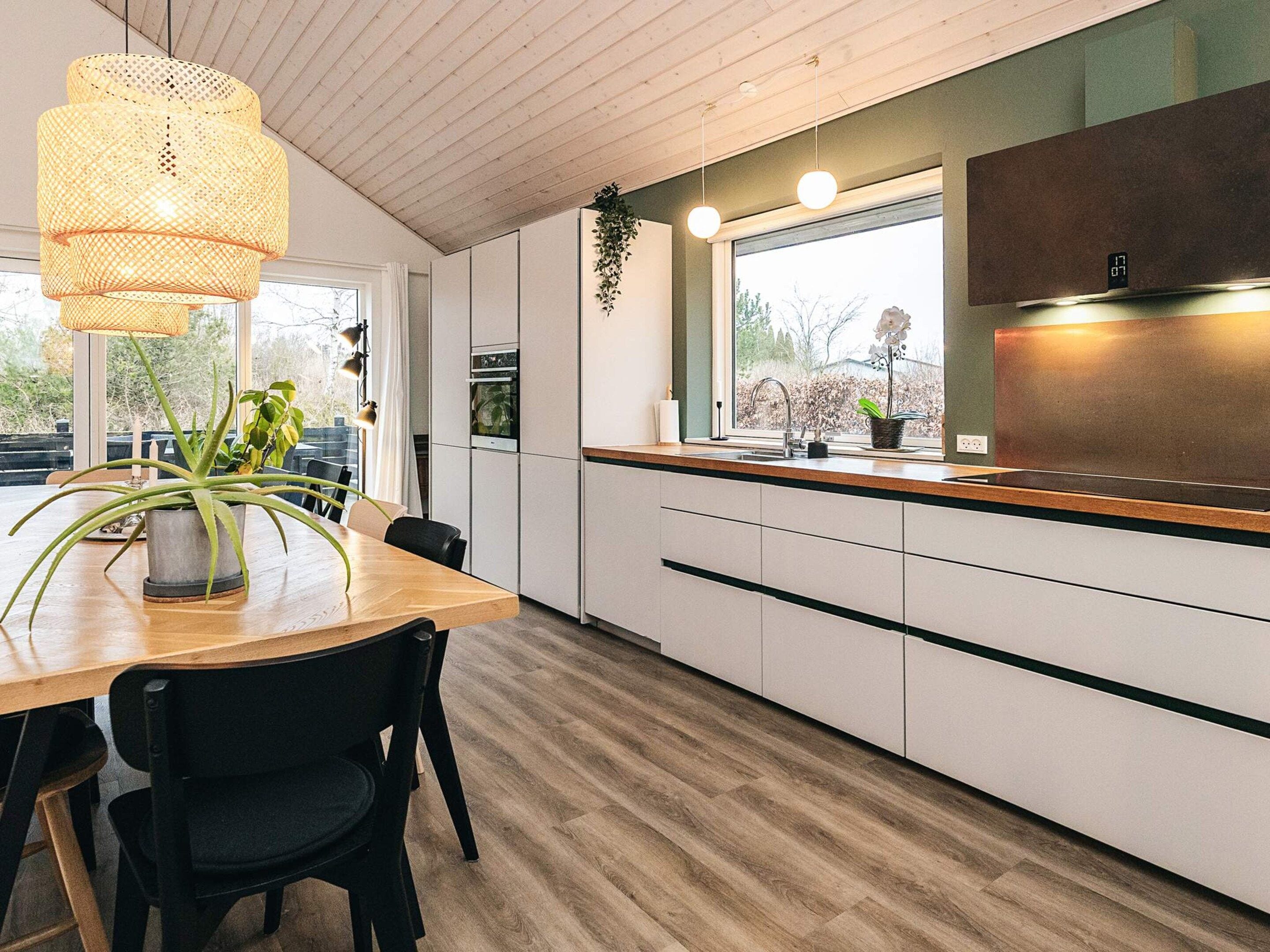 A modern kitchen with a wooden countertop, white cabinets, and a hanging light fixture.