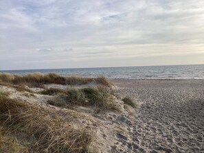 Una spiaggia con dune di sabbia e un mare calmo sotto un cielo nuvoloso.