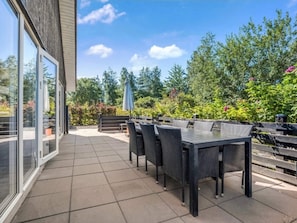 An outdoor patio with a dining table and chairs, surrounded by greenery and a clear sky. - 4 Star Holiday Home in Vaeggerlose (Vaeggerlose)