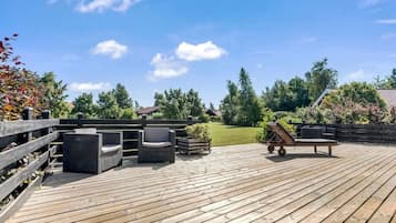 A wooden deck with outdoor furniture, a wooden fence, and a view of a grassy yard with trees and a house in the background.