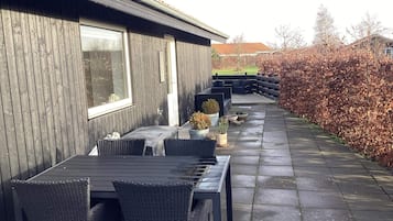 An outdoor patio with a table and chairs, a wooden wall, and a hedge.