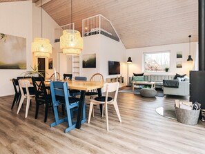 Ein modernes Wohnzimmer mit Essbereich, Holzboden und einem Schlafbereich mit Balkon.