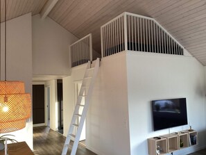 A loft-style room with a TV, wooden ladder, and a white railing. - 4 Star Holiday Home in Vaeggerlose (Vaeggerlose)