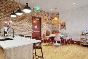 A modern kitchen with a brick wall, wooden flooring, and a central island with a sink. - The Gisele: 4BR/3BA for 8 | Pool + Streetcar Stop (New Orleans)