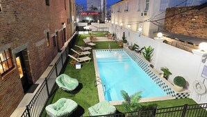 Una piscina con lettini e un piccolo giardino, circondata da edifici.