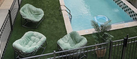A swimming pool with a checkered border, surrounded by artificial grass and lounge chairs.