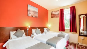 Ein Hotelzimmer mit zwei Betten, roten Vorhängen, einem Fenster mit Blick und einem Bild an der Wand.
