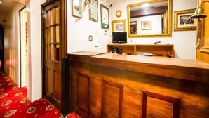 Ein Empfangsbereich mit Holztresen, gerahmten Bildern an der Wand, einer Uhr und einem Teppichboden in Rot.