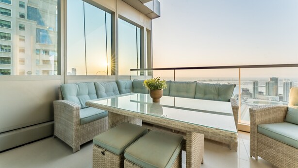 Een modern balkon met rieten meubilair, een glazen tafel en uitzicht op de stad.