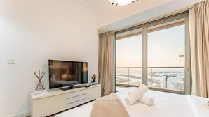 Een moderne hotelkamer met een groot bed, een televisie op een witte dressoir en een balkon met uitzicht op de stad.