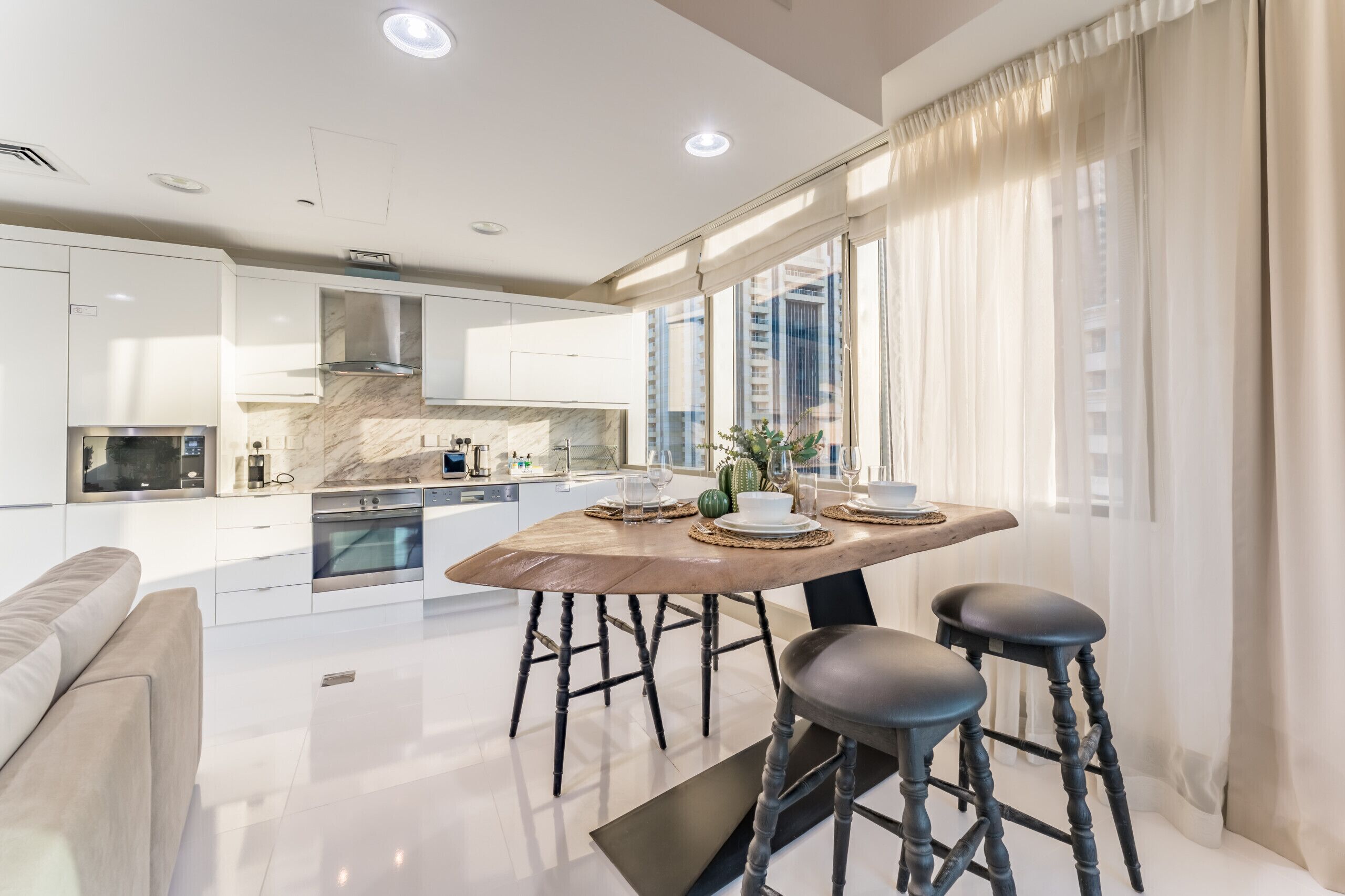 A modern kitchen with white cabinets, a marble backsplash, and a dining area with a wooden table and stools.