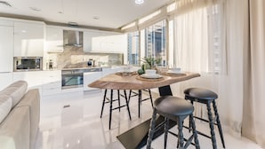 Een moderne keuken met witte kastjes, een marmeren spatwand en een eethoek met een houten tafel en krukken.
