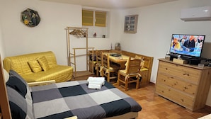 Een kleine kamer met een bed, een slaapbank, een houten eettafel met stoelen, een televisie en een dressoir.