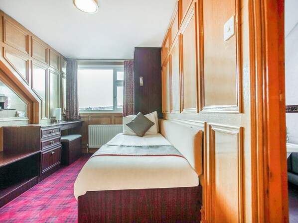 A hotel room with a bed, a dresser, a window with curtains, and a view of the outside. - Standard Single Room (Gateshead)
