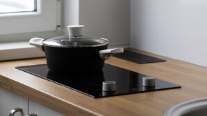 Een keuken met een zwarte pan op een inductiekookplaat, een houten aanrecht, een witte muur en een hangende plant.