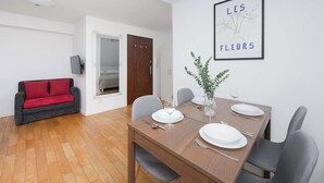 Een eethoek met een houten tafel gedekt voor vier personen, een rode bank en een lijst met een afbeelding aan de muur.