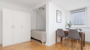 Een compacte slaapkamer met een bed, een witte garderobe en een klein bureau met stoelen.