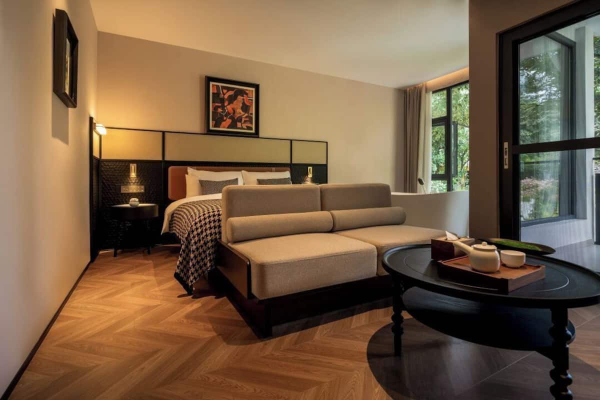 Ein modernes Hotelzimmer mit einer Couch, einem Nachttisch, einer Lampe und einem großen Fenster.