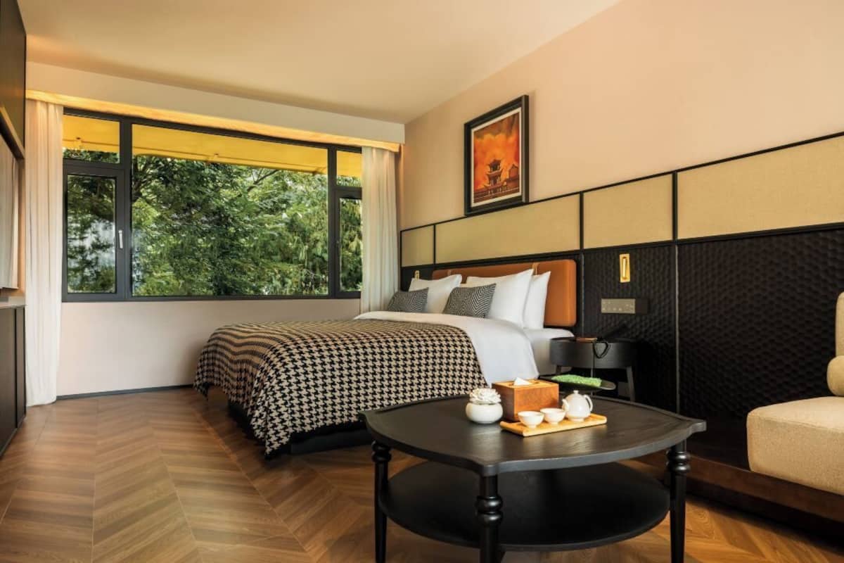 Ein Hotelzimmer mit einem großen Bett, einem Nachttisch mit einer Teekanne und Blick auf Grünflächen.
